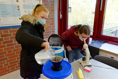 Chemie praktisch: Mit einer Camping-Waschmaschine, einem Filter und dem Mikroskop zeigen Katja (rechts) und Amelie Mikroplastik-Abrieb im Wasser - das gibt es wirklich und es ist ein Problem. Foto: Gemeinde Saerbeck